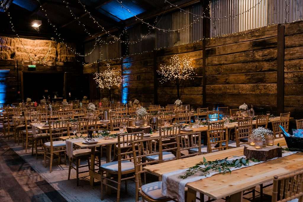 interior photo of long wooden tables  and bare wooden chairs dressed for a wedding meal in Harelaw Farm