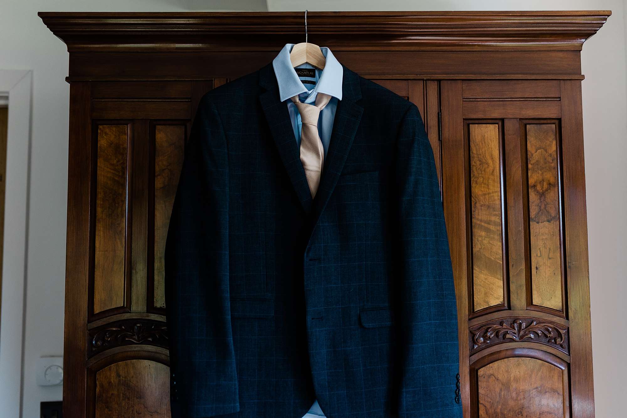 gents wedding suit, shirt and tie hanging up on a wooden wardrobe