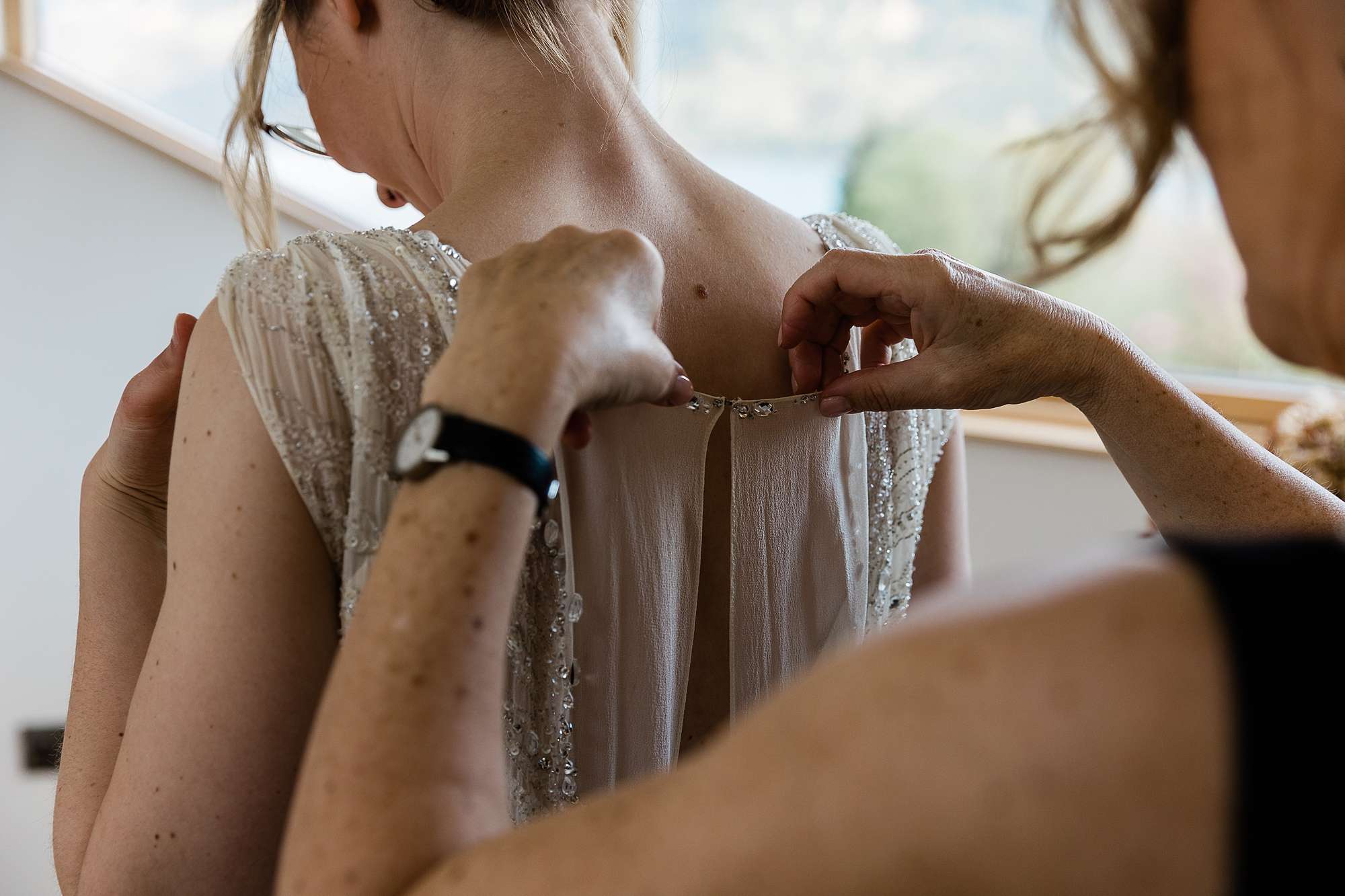 bride having her dress fastened at the back 