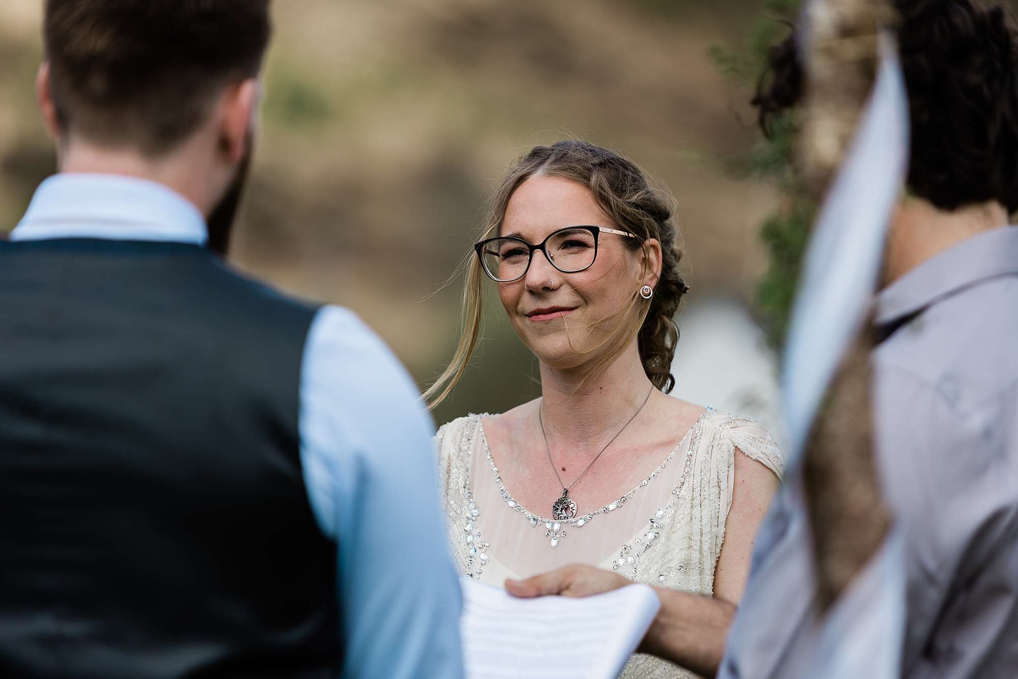 bride in glasses smiling at groom during wedding ceremony