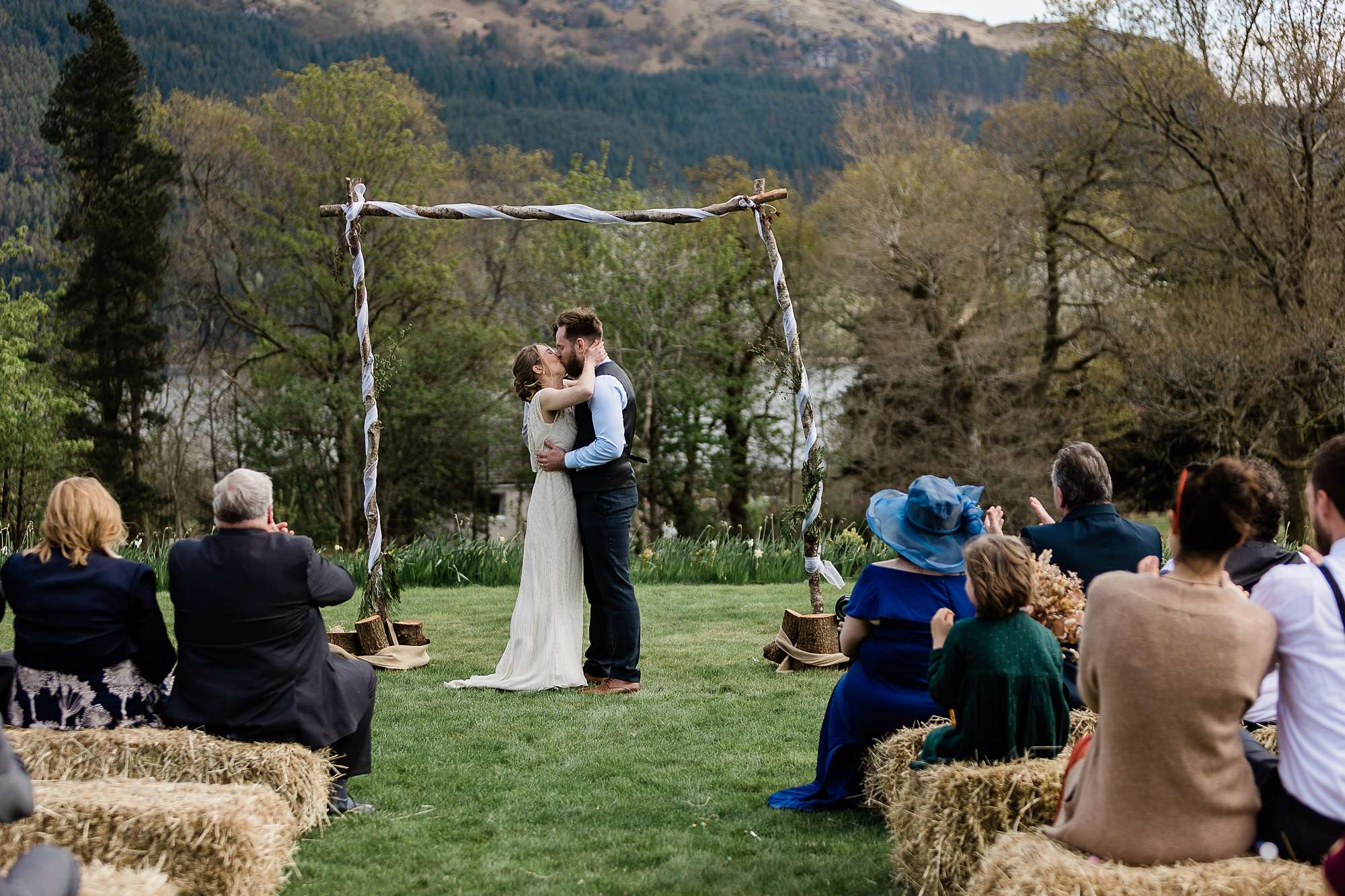 bride and groom kissing under a rustic wooden arch at outdoor wedding ceremony at Carrick Castle estate