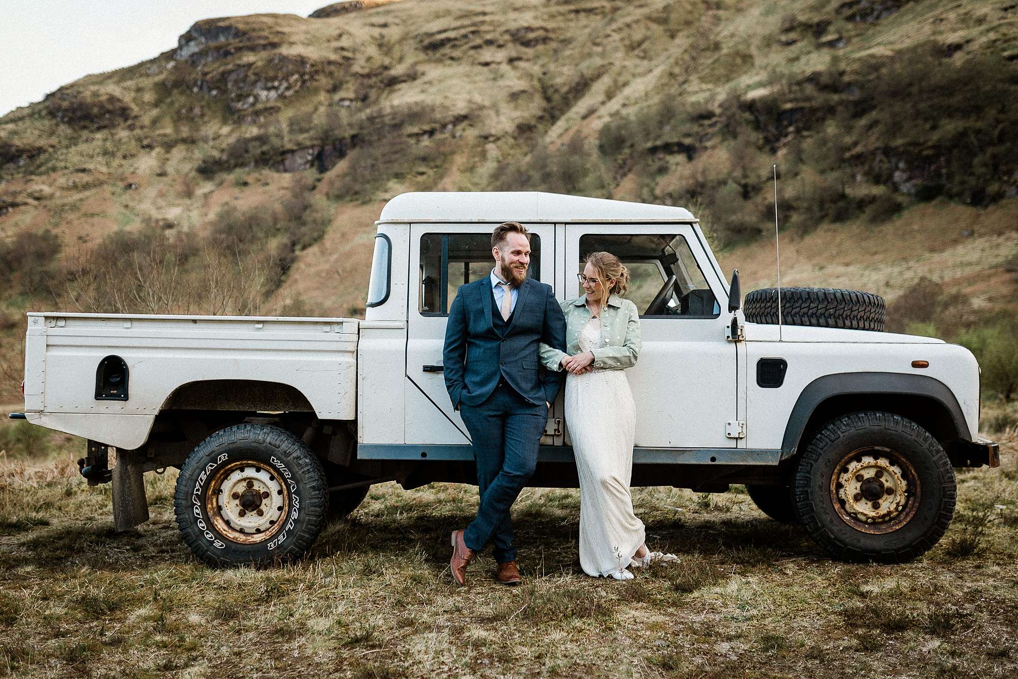 bride and groom standing by a white land rover