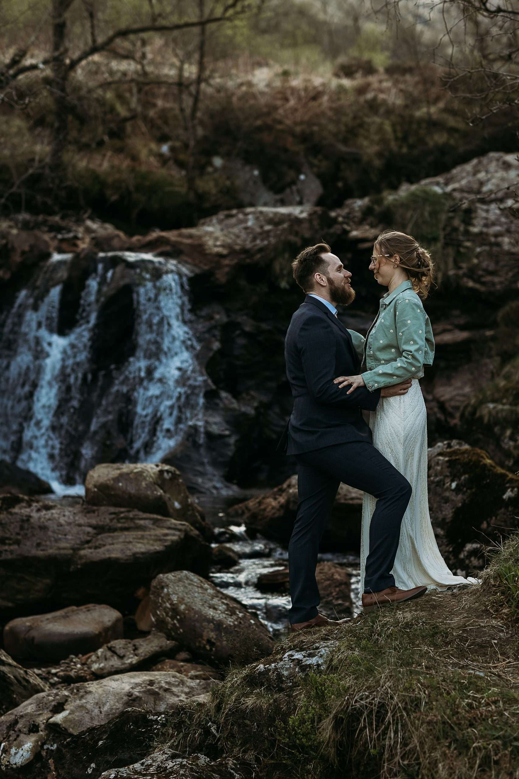groom standing in front of bride in front of a waterfall