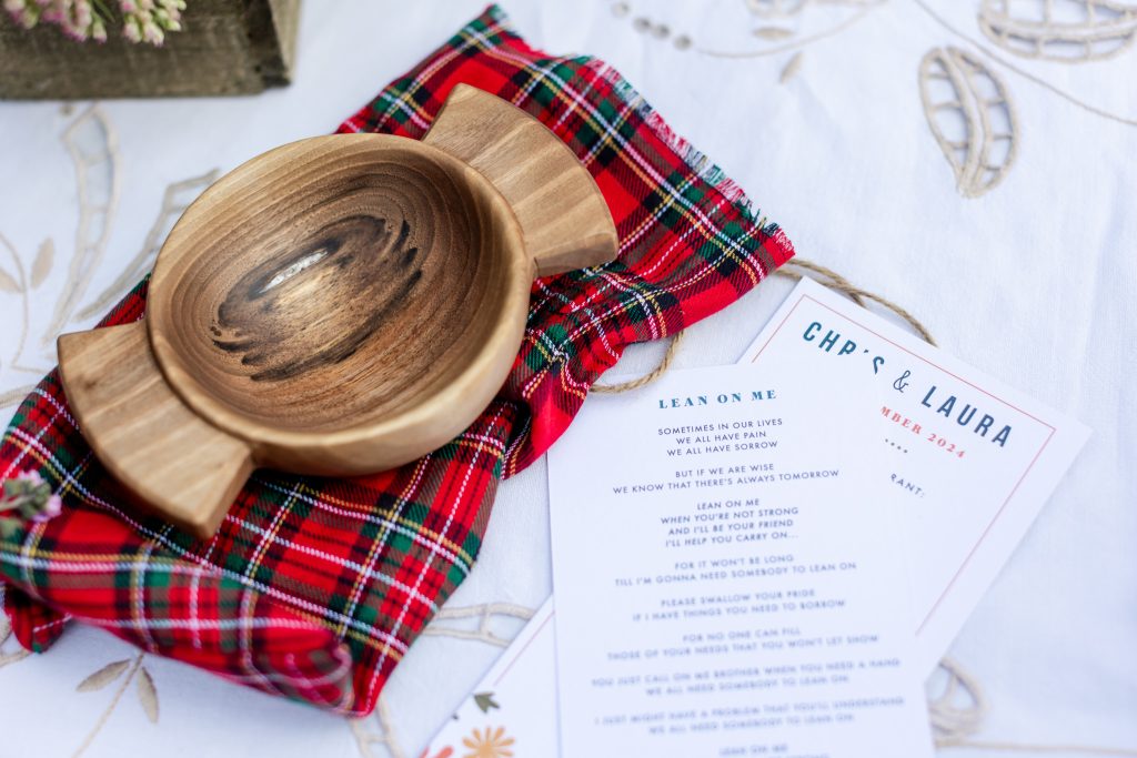 words to Lean On Me for a wedding, next to a red tartan handfasting ribbon and a wooden quaich bowl