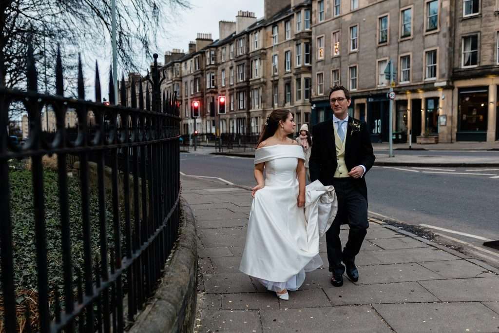 groom holding bride's dress walking down the street