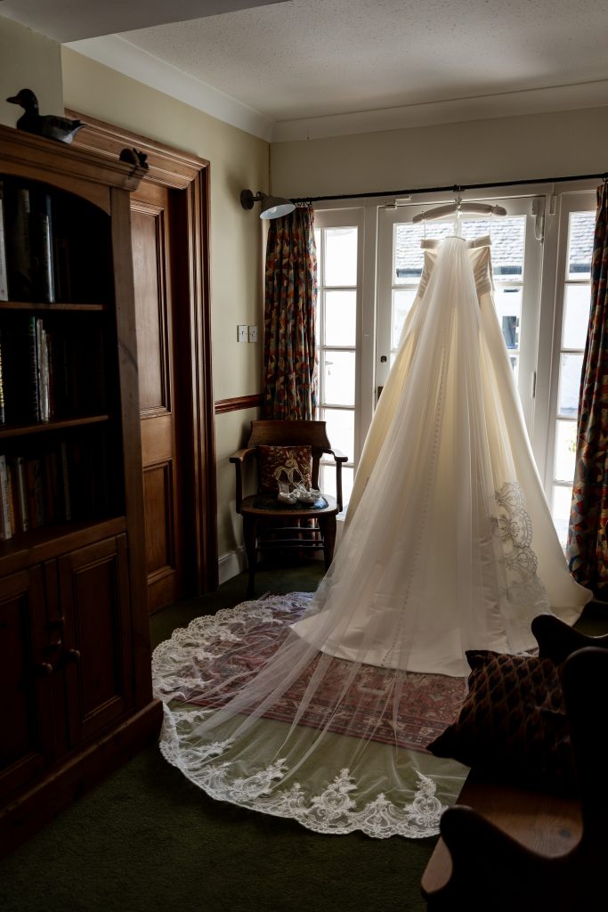 wedding dress with veil fanned out hanging over a glass door in a dark room