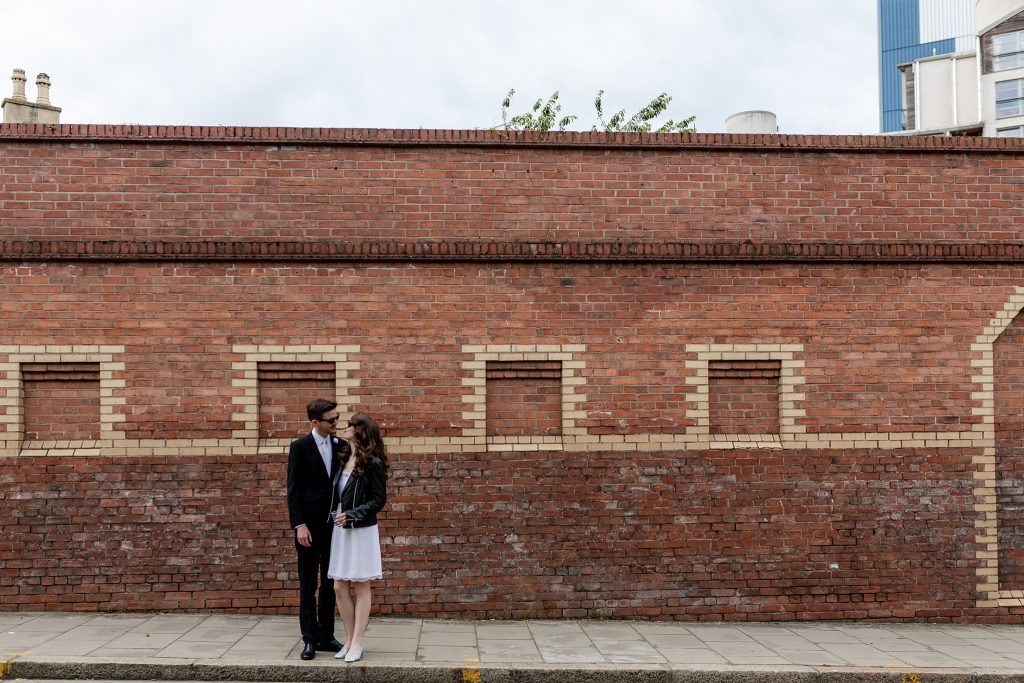 bride and groom embracing next to a red brick wall in leith