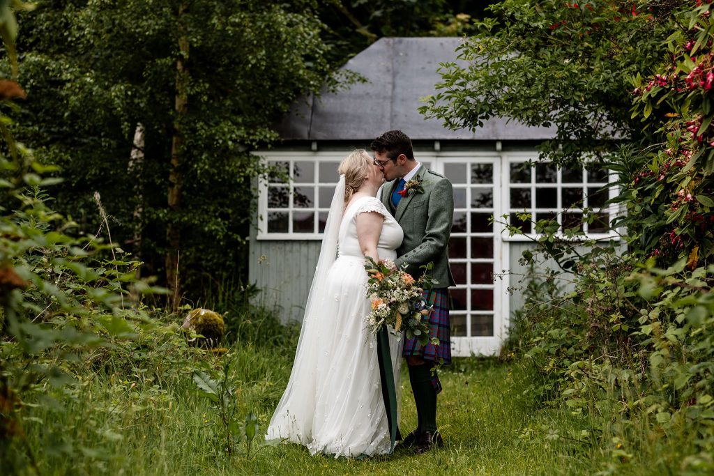 bride and groom kissing in front of green wooden summer house in the woodlands