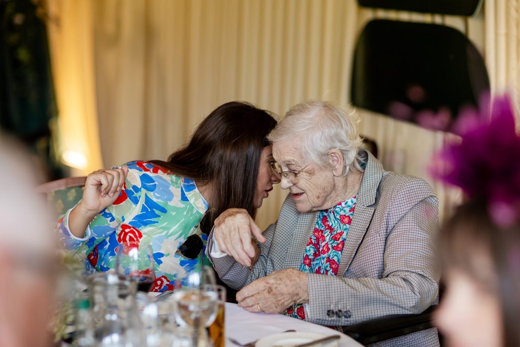 woman whispering into an older woman's ear at a table