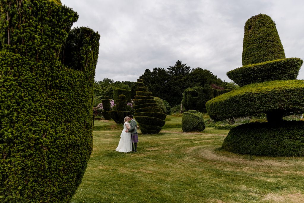 bride and groom standing surrounded by quirky topiary