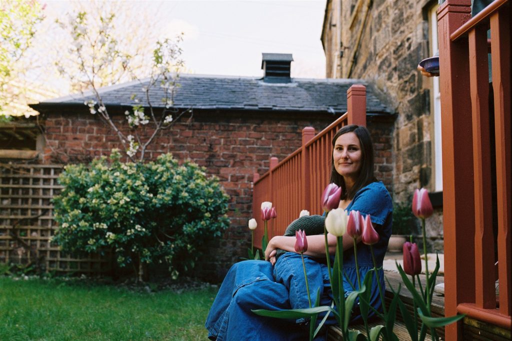 35mm film image of a woman breastfeeding in her garden next to some tulips during a during a documentary family photography session in glasgow