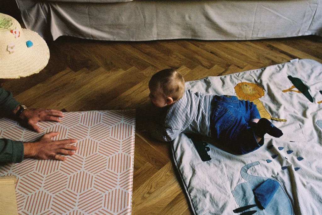 35mm film image of a baby crawling across a blanket on a wooden floor during a documentary family photography session in glasgow