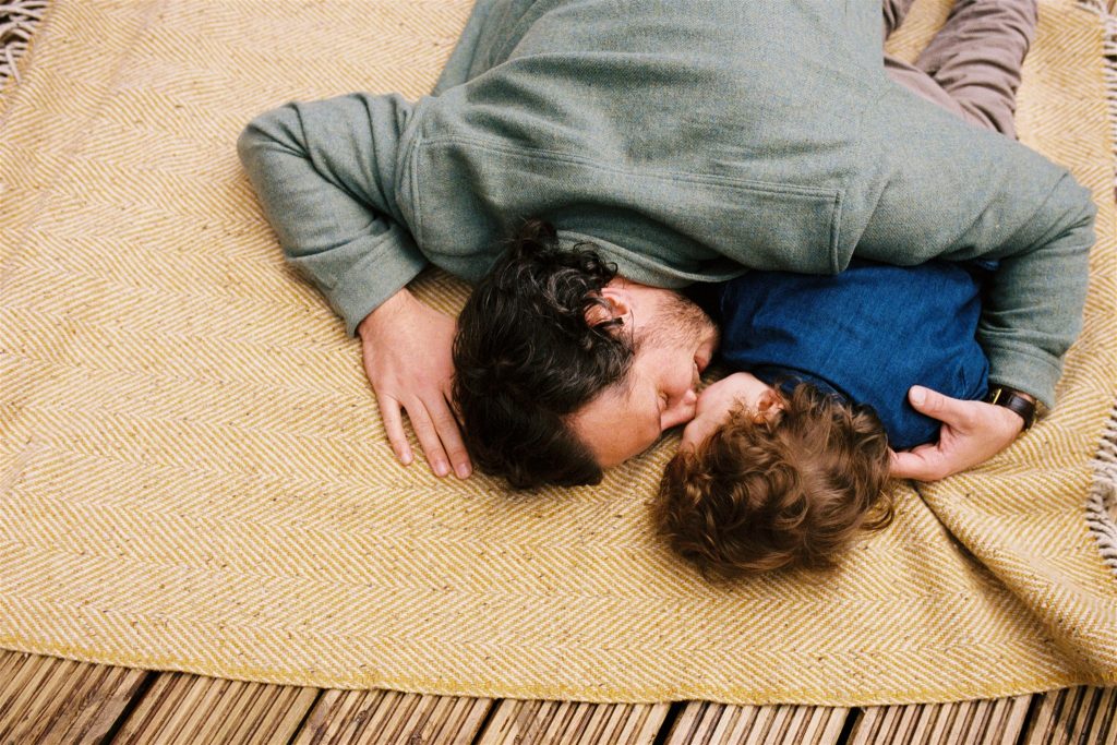 35mm film image of a man lying on a yellow blanket next to his small son during a documentary family photography session in glasgow