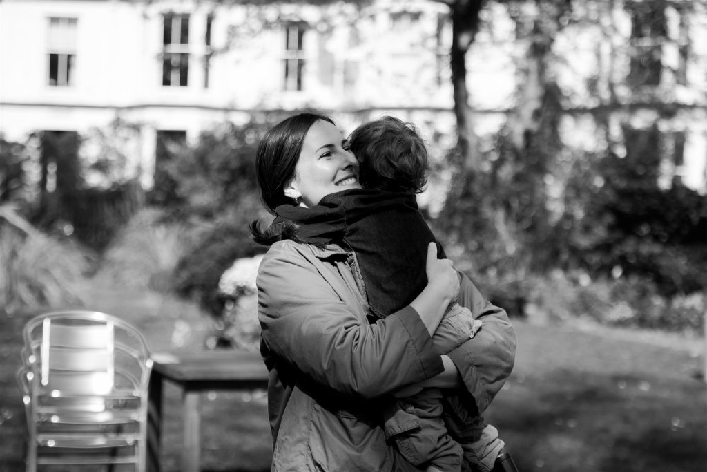mother hugging a small child outside in a communal garden during a documentary family photography session in glasgow