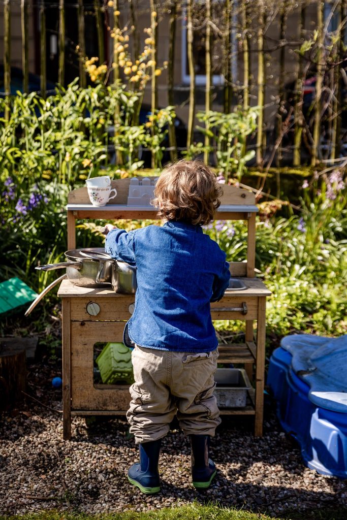 little boy in a denim shirt playing in a mud kitchen in the sunshine