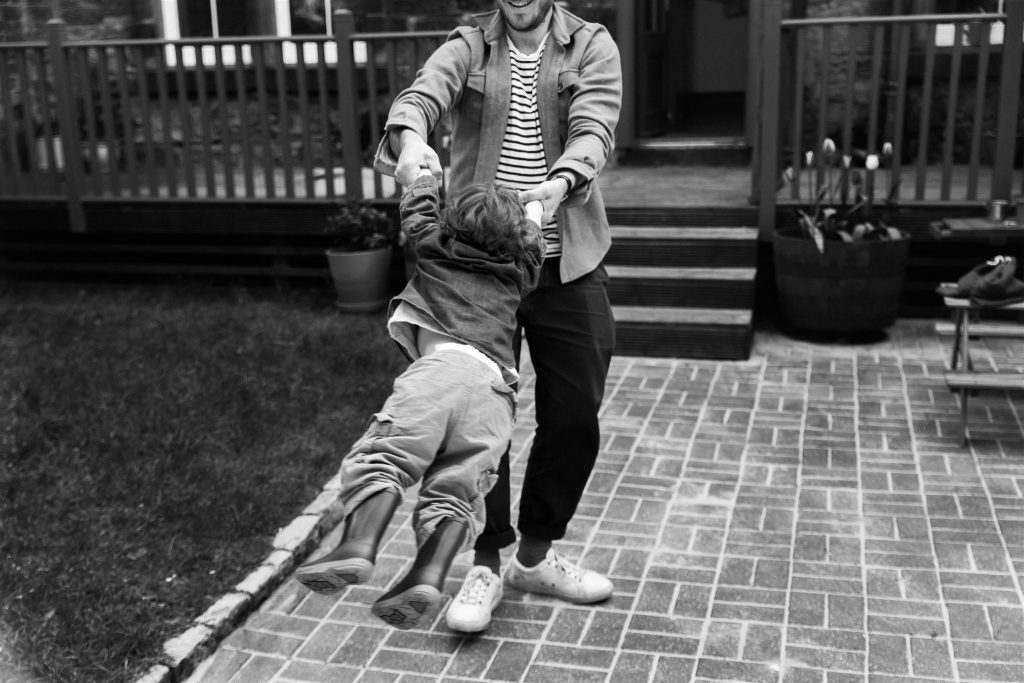 man swinging a child around a garden during a documentary family photography session in glasgow