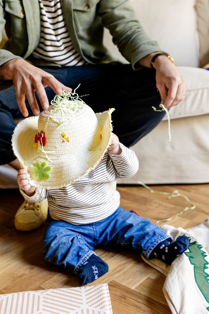 baby wearing a yellow straw bonnet sitting on a wooden floor during a documentary family photography session in glasgow
