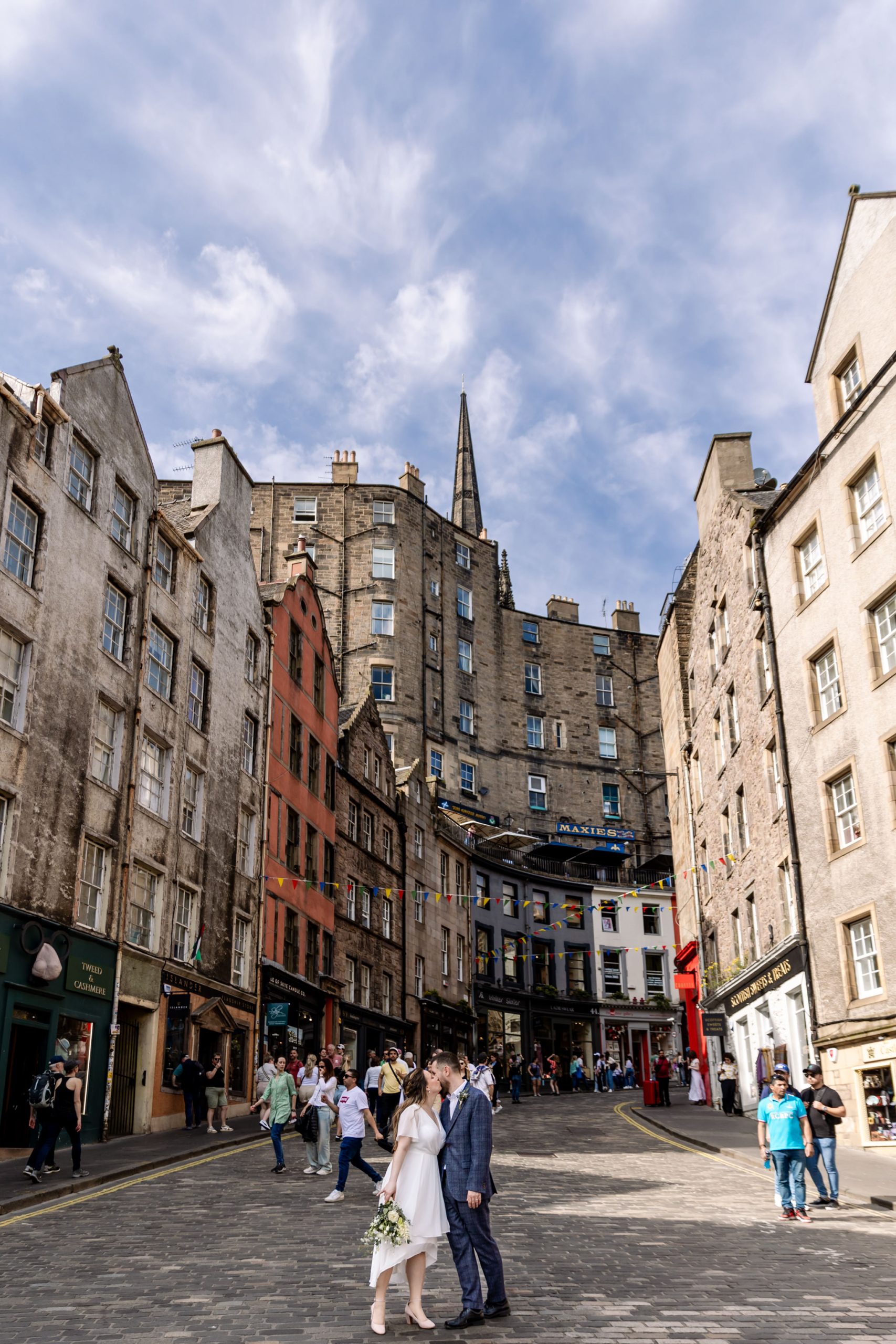 bride and groom embracing at foot of Victoria Street in Edinburgh with bunting and multicolour shops 