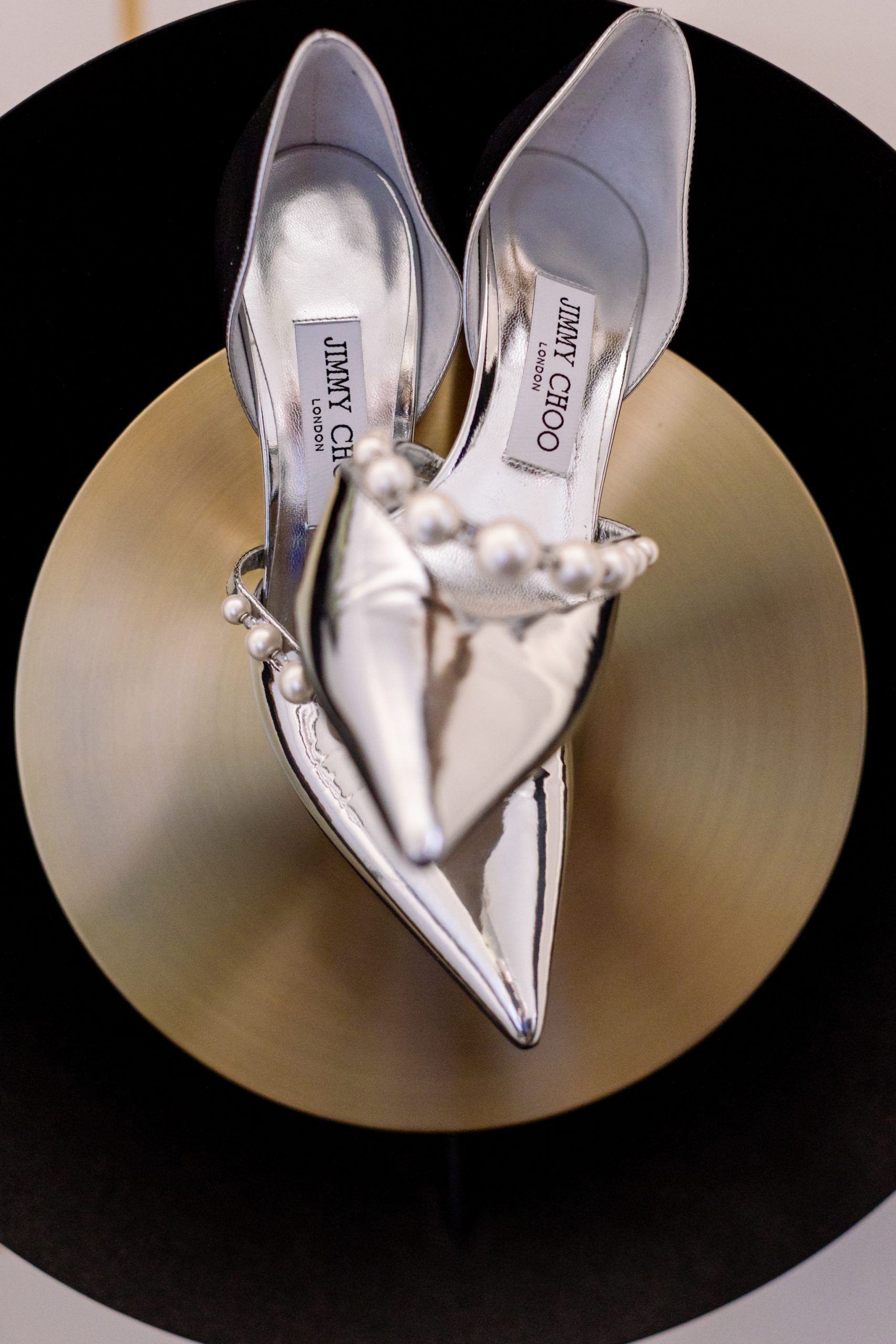 silver Jimmy Choo shoes on a gold disk