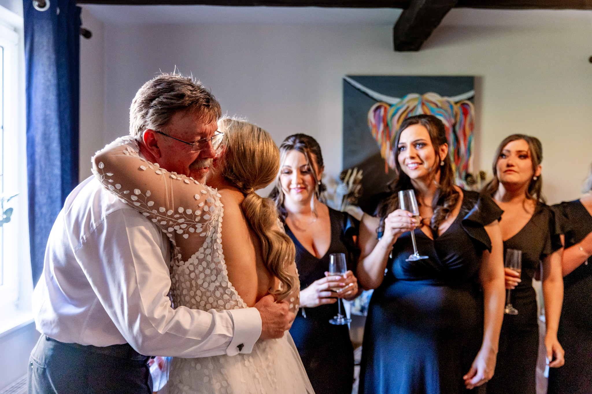 father of the bride embracing his daughter while being watched by bridesmaids 