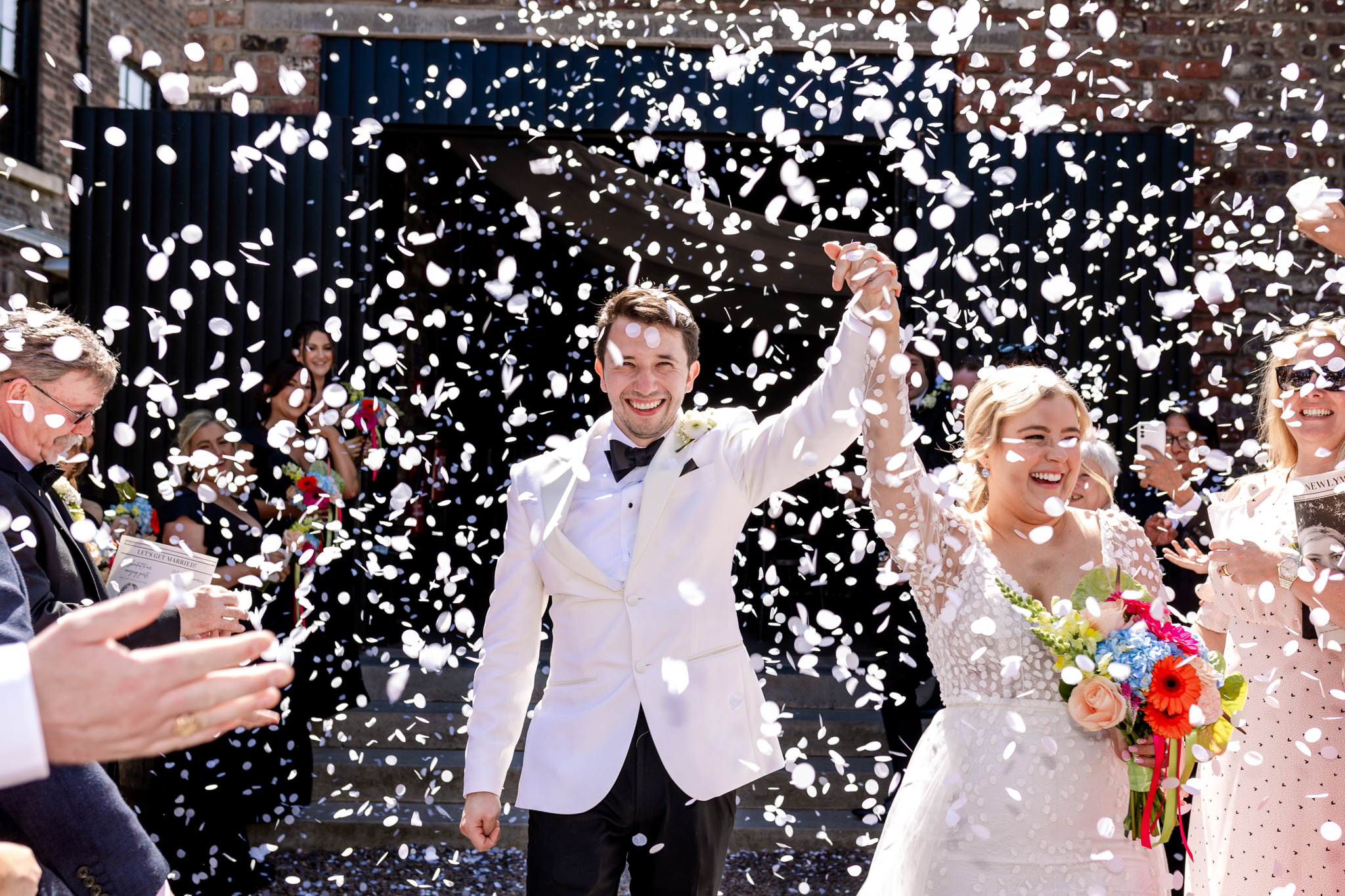 bride and groom walking out with their arms in the air into a shower of white confetti at Engine Works Wedding in Glasgow