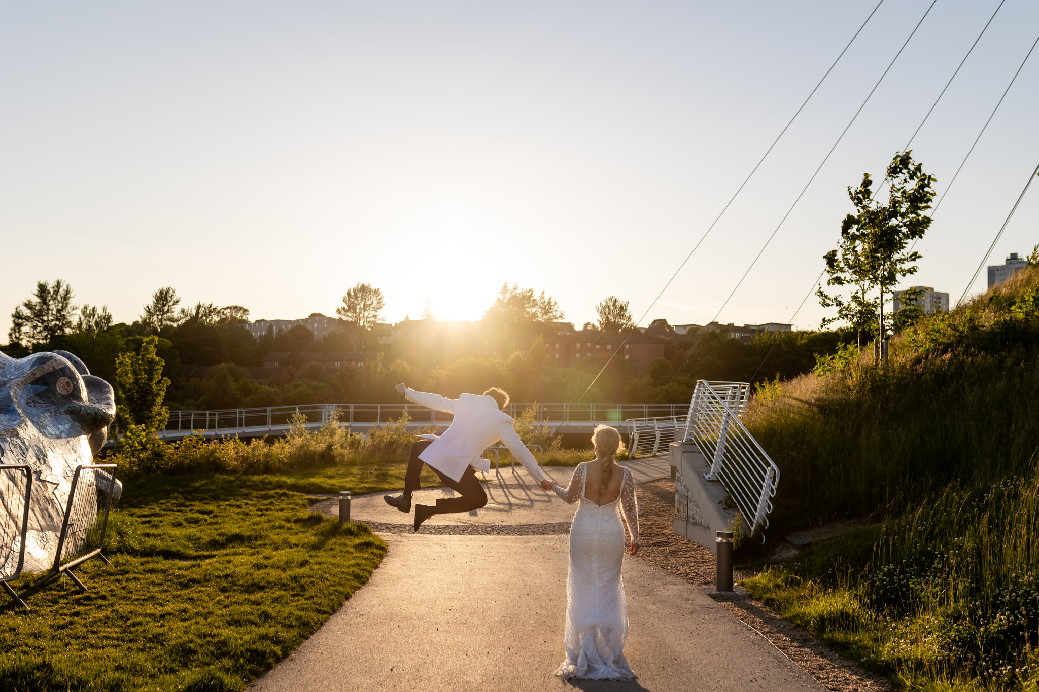 groom jumping in the air and clicking his heels together, while holding hands with bride