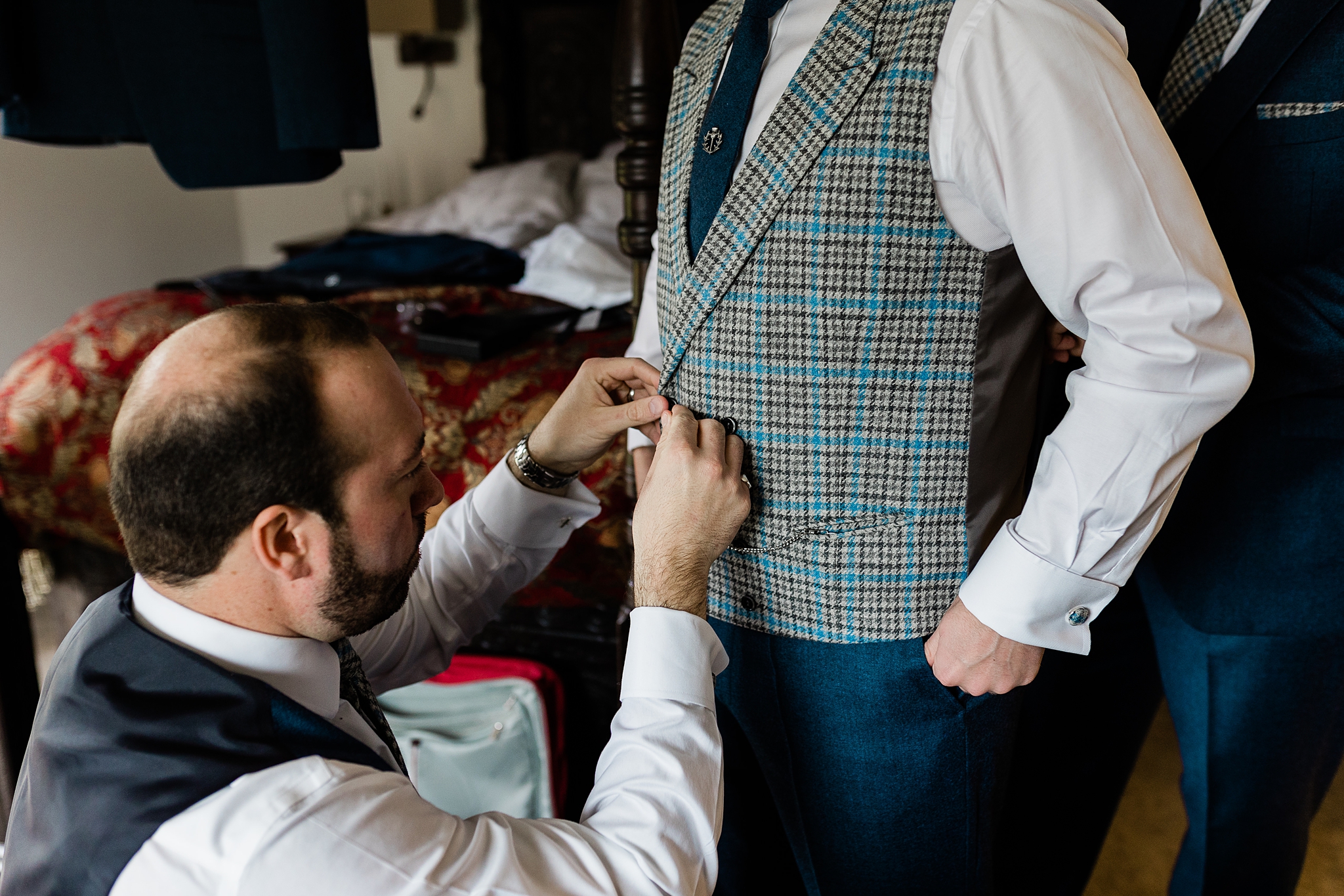 man helping another man to fasten his houndstooth waistcoat