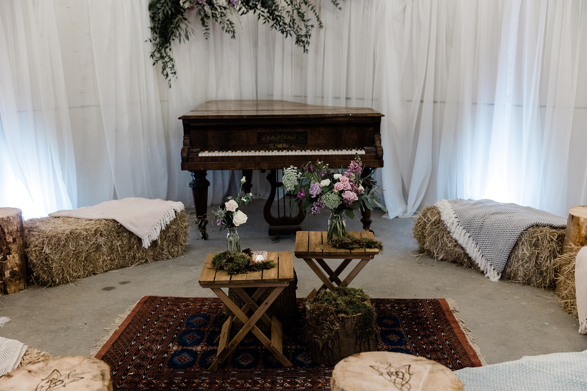baby grand piano, rugs, hay bales and wooden tables at a at a wedding in the barn at Carrick Castle Estate