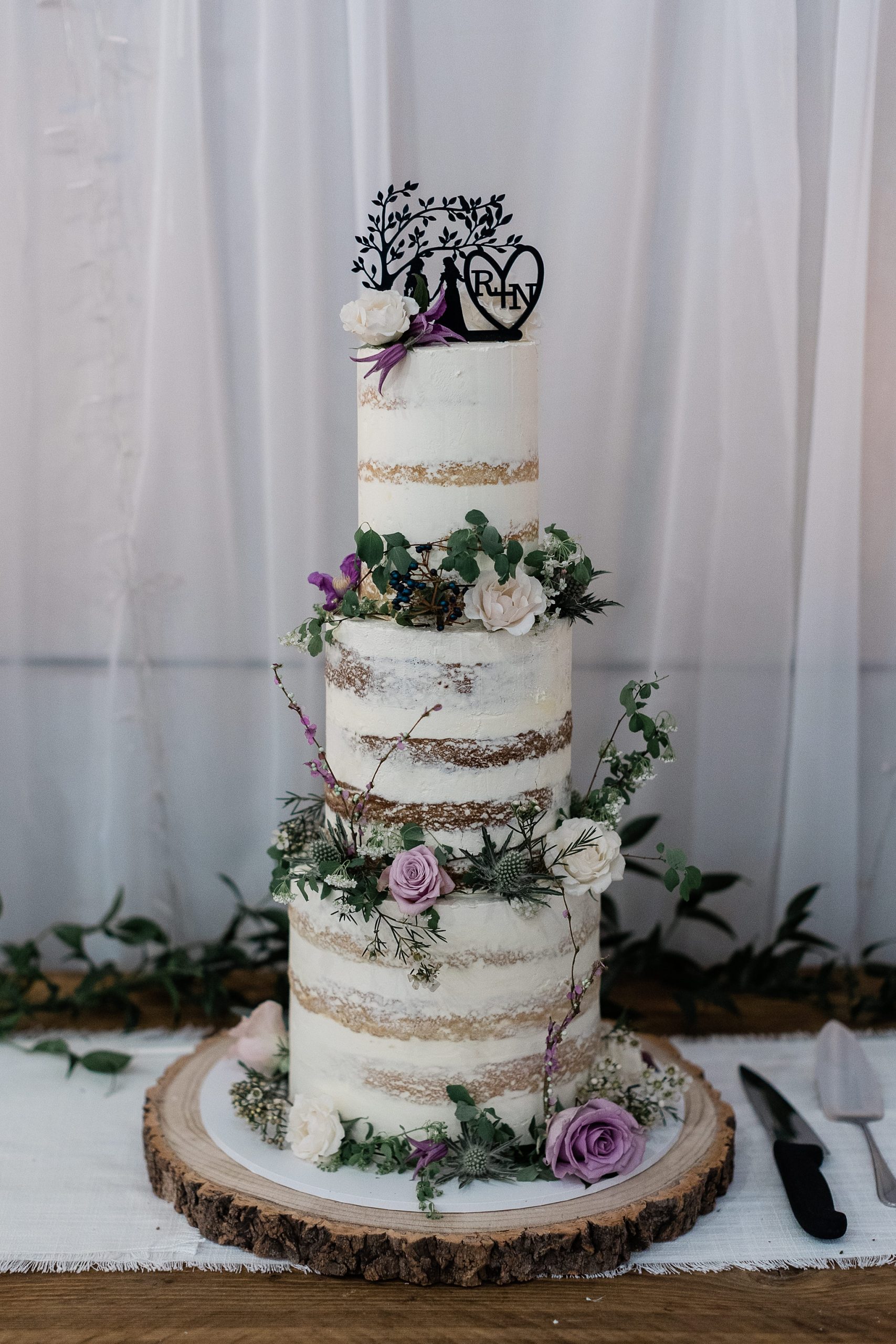 Three tier naked wedding cake decorated with flowers and a black cut out sign on the top, by the little Cake Parlour at a celtic folklore theme wedding in Scotland