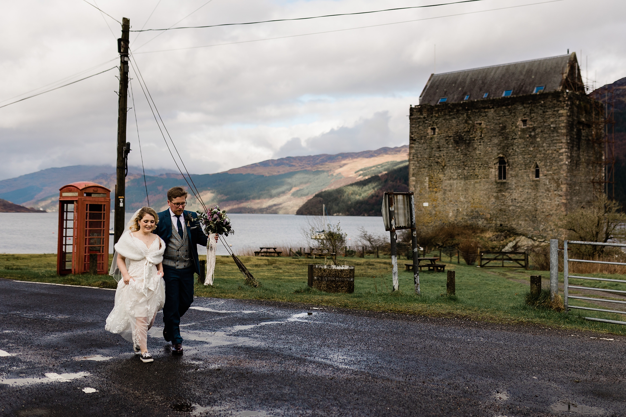 bride and groom walking along a road with Scottish castle in background