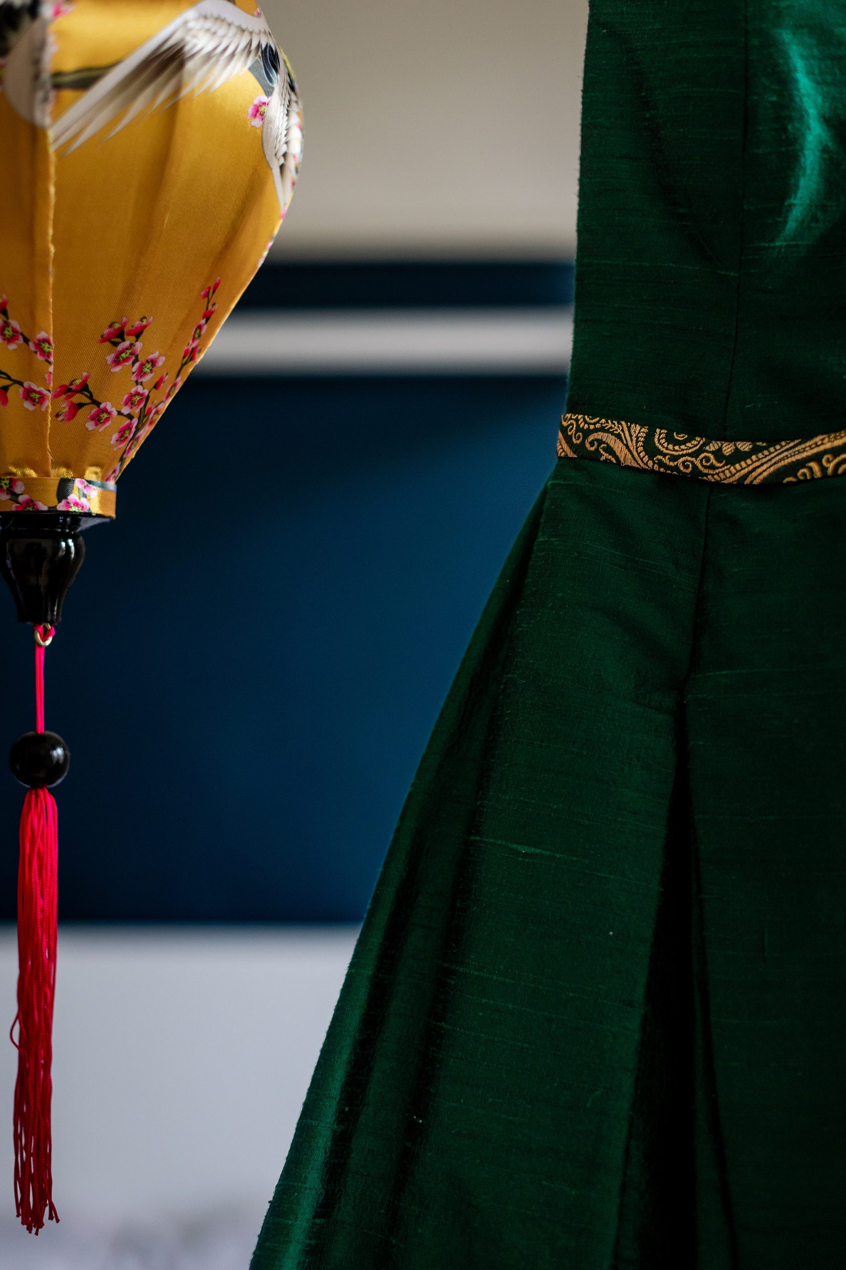 side of a green silk Flossy and Dossy Wedding dress next to a yellow lantern in front of a navy wall 