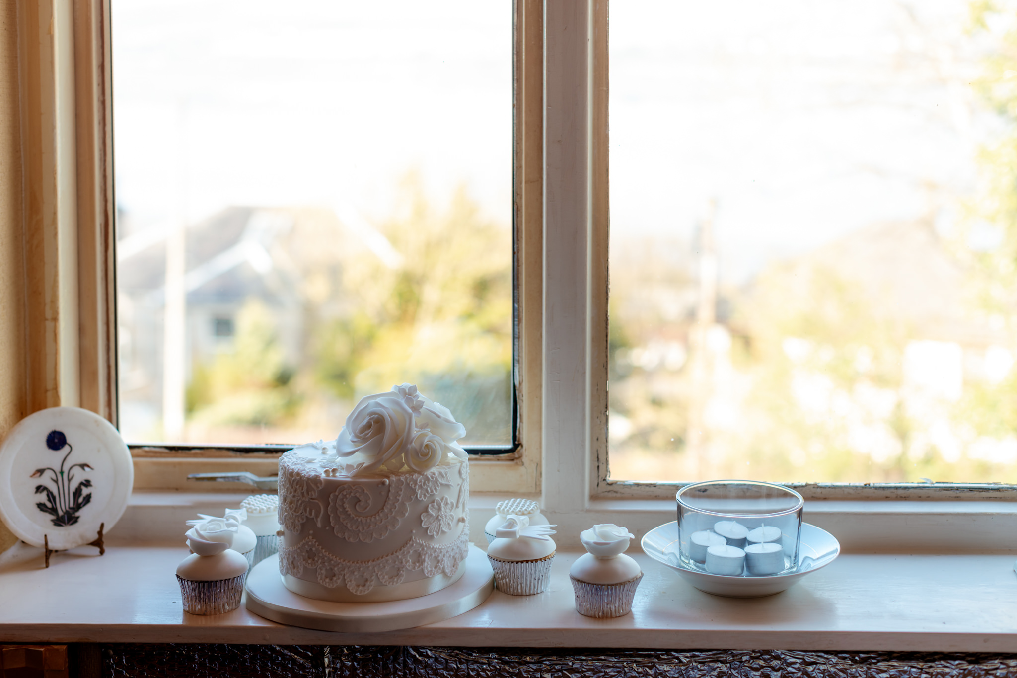 white wedding cake and cupcakes on a window sill