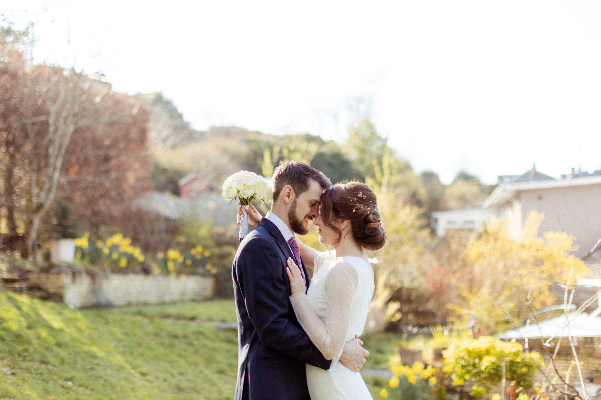 bride and groom embracing in the sunshine in a garden and touching foreheads