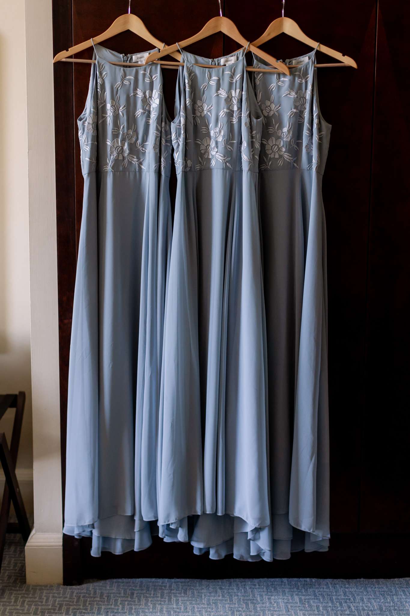 three pale blue long bridesmaid dresses hanging on wooden hangers