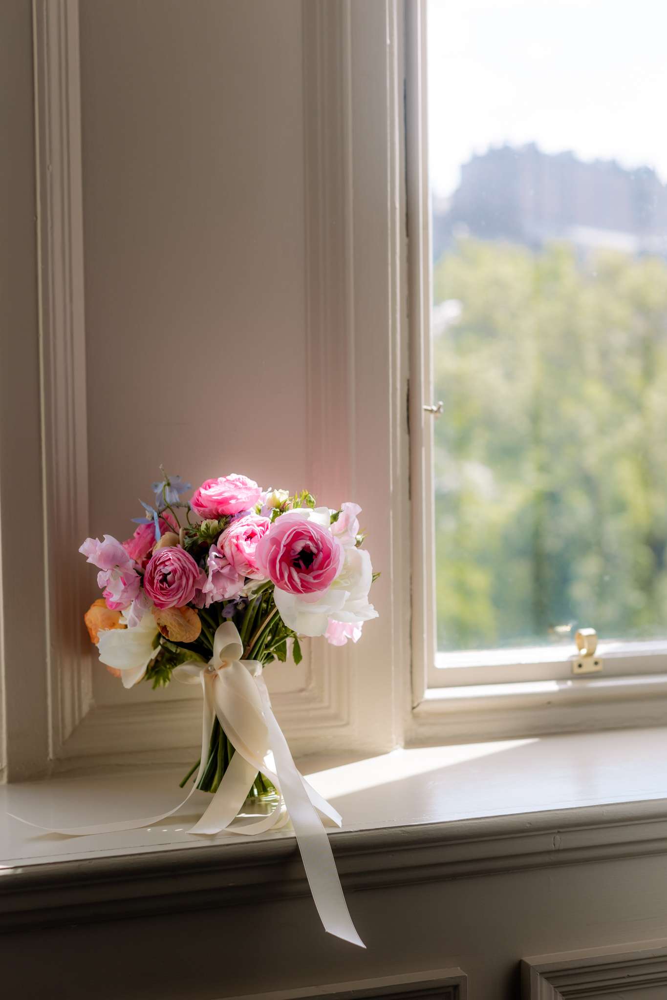 pink and white wedding bouquet with ivory ribbon, next to a window overlooking Edinburgh Castle