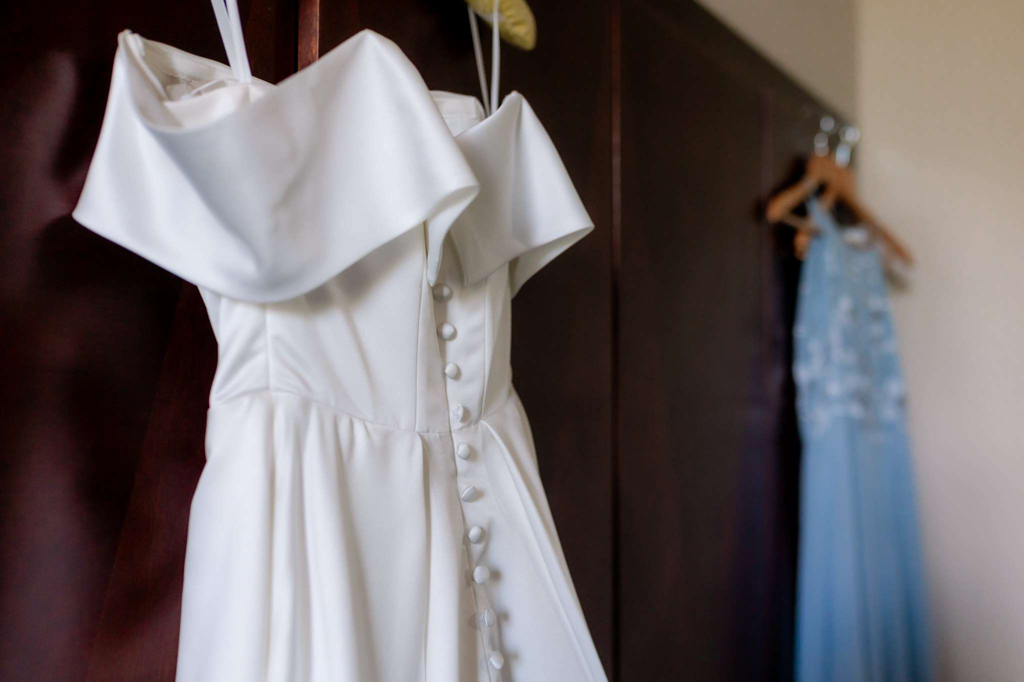 white wedding dress hanging on a wardrobe near some blue bridesmaids dresses
