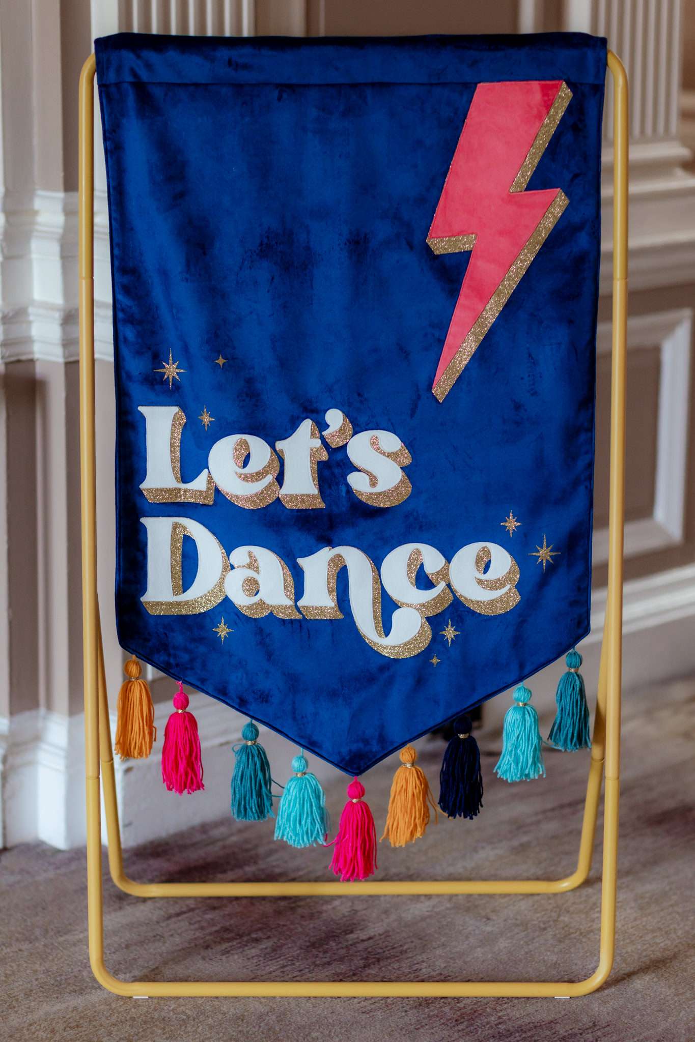 blue and pink and gold velvet banner with tassles on a gold frame reading "let's dance" with a lightning bolt