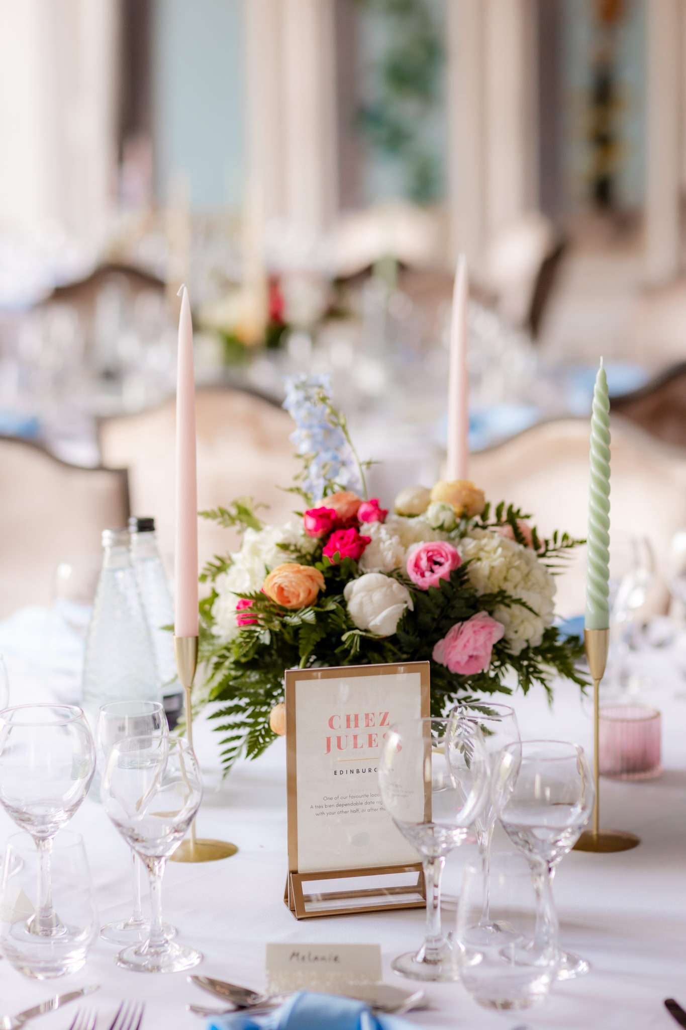 pale pink and green candles, and pink and white flowers on a wedding table with a framed table place name reading Chez Jules Edinburgh