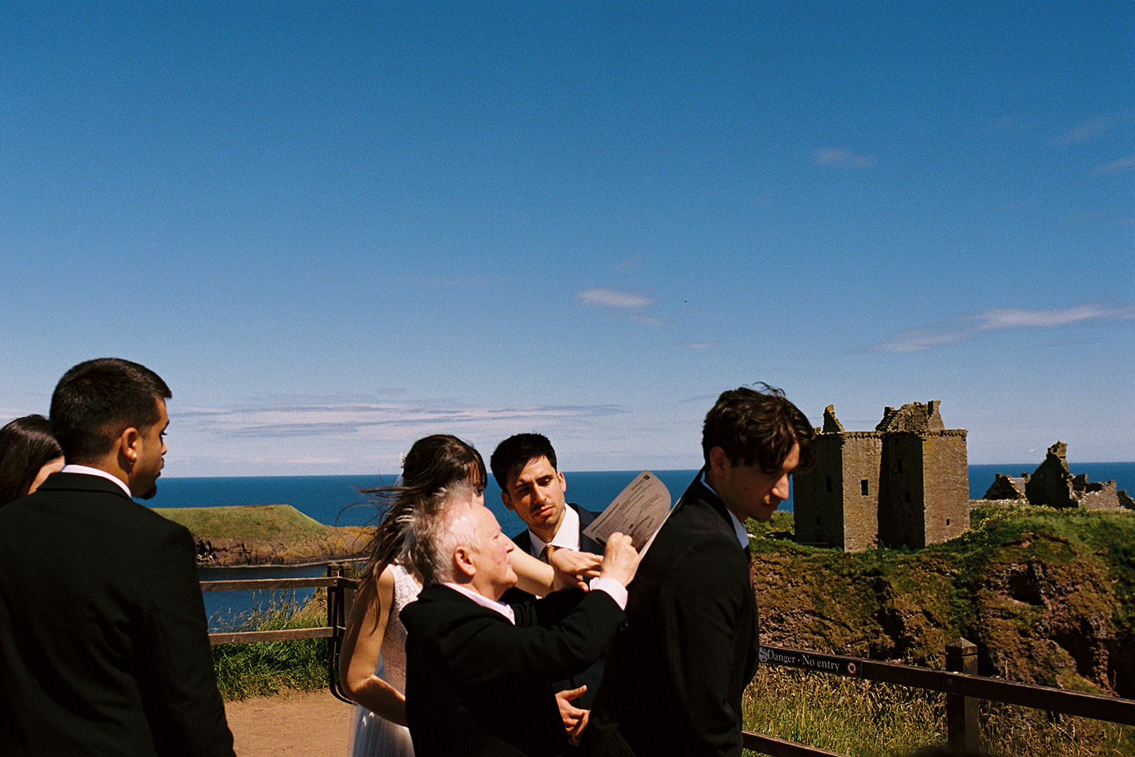 bride signing wedding schedule on the back of a guest, at a wedding ceremony at Dunnottar Castle