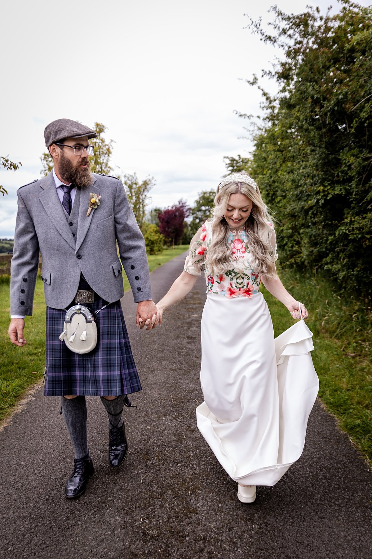 bride and groom holding hands and walking along a path