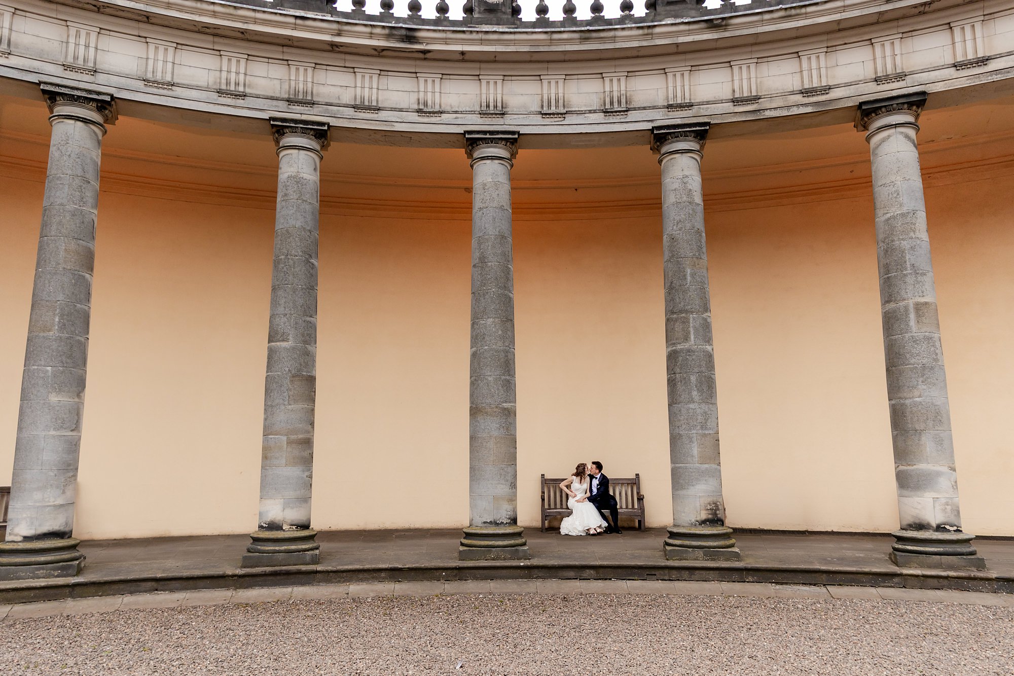 bride and groom kissing on a bench under the collonades at Hopetoun House