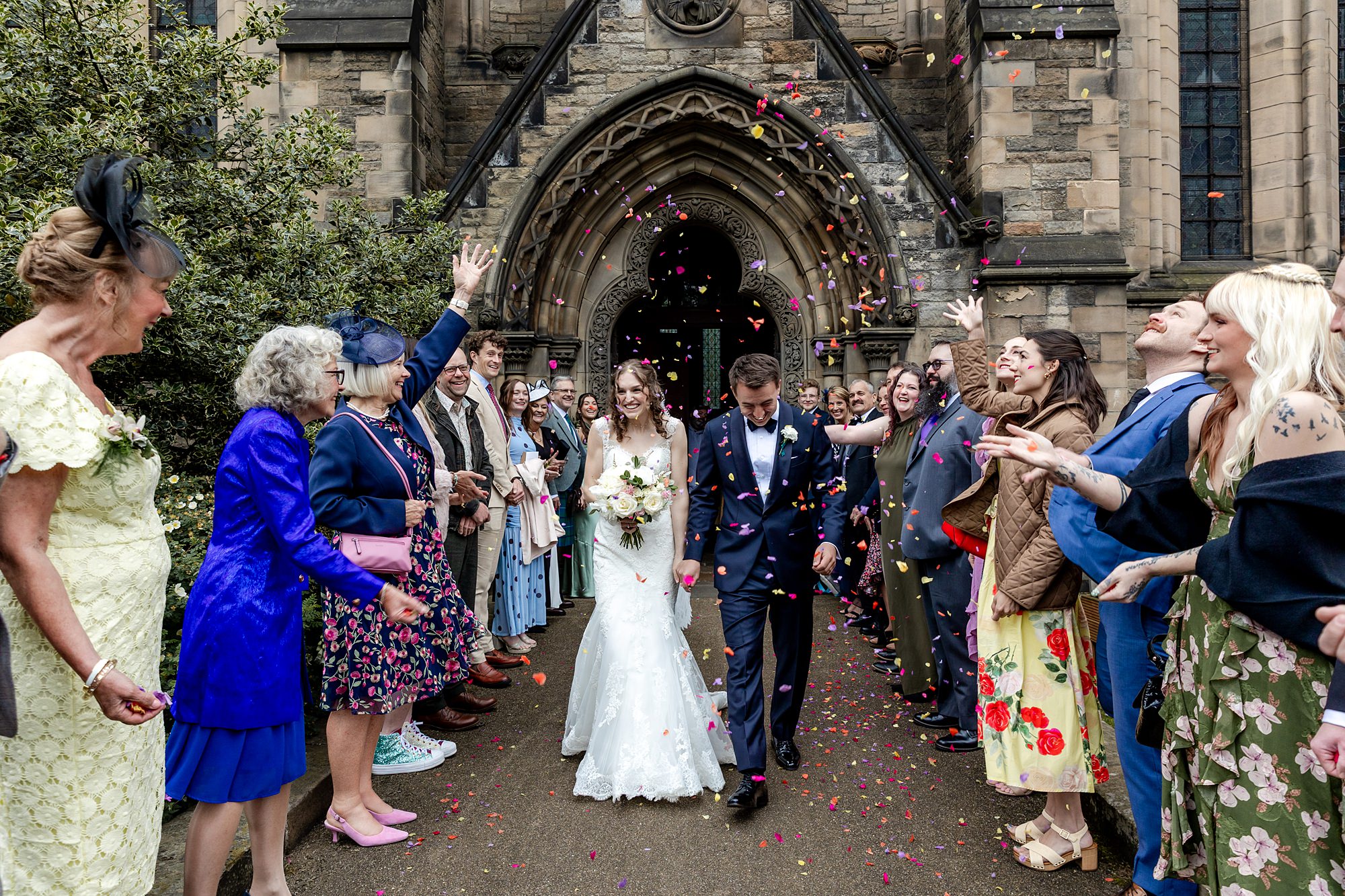 bride and groom walking through confetti outside St Mary's Episcopal Church in Edinburgh with guests lined up on either side