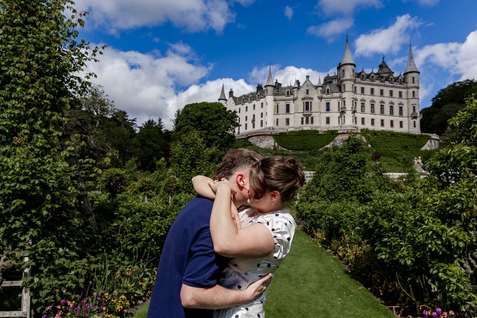woman embracing her fiance outside Dunrobin Castle, in the garden after he proposes in the Scottish Highlands. 