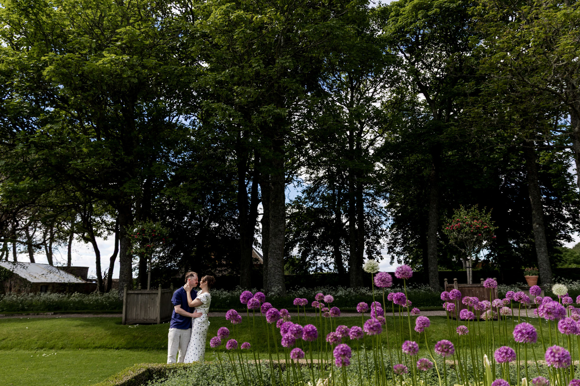 couple embracing with woodlands behind them and alum flowers in the foreground