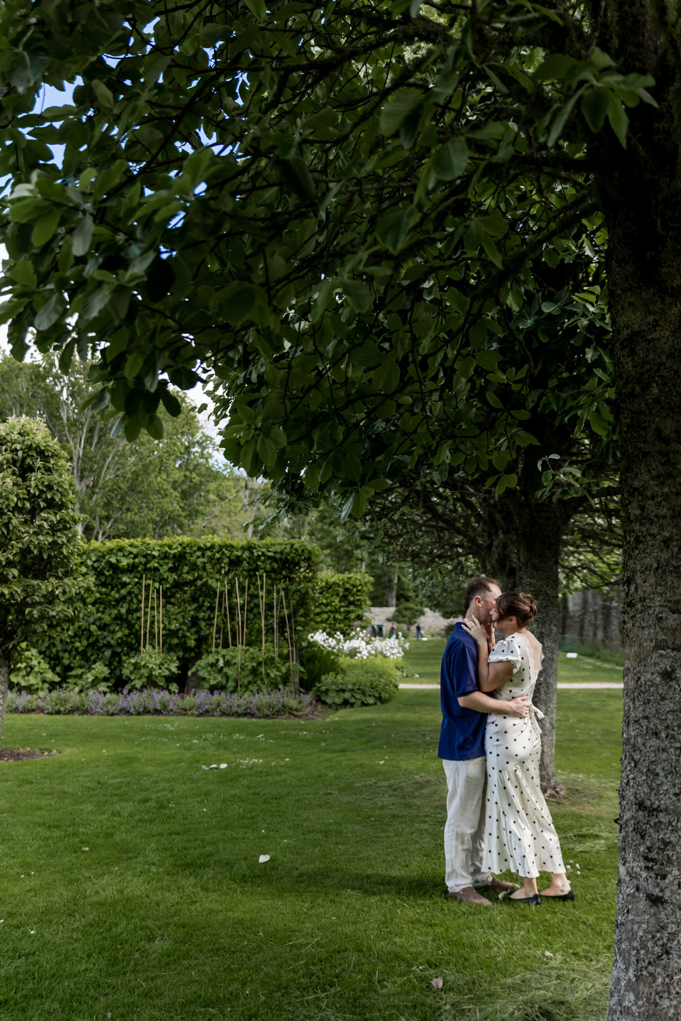 couple kissing under an avenue of trees in a castle garden 