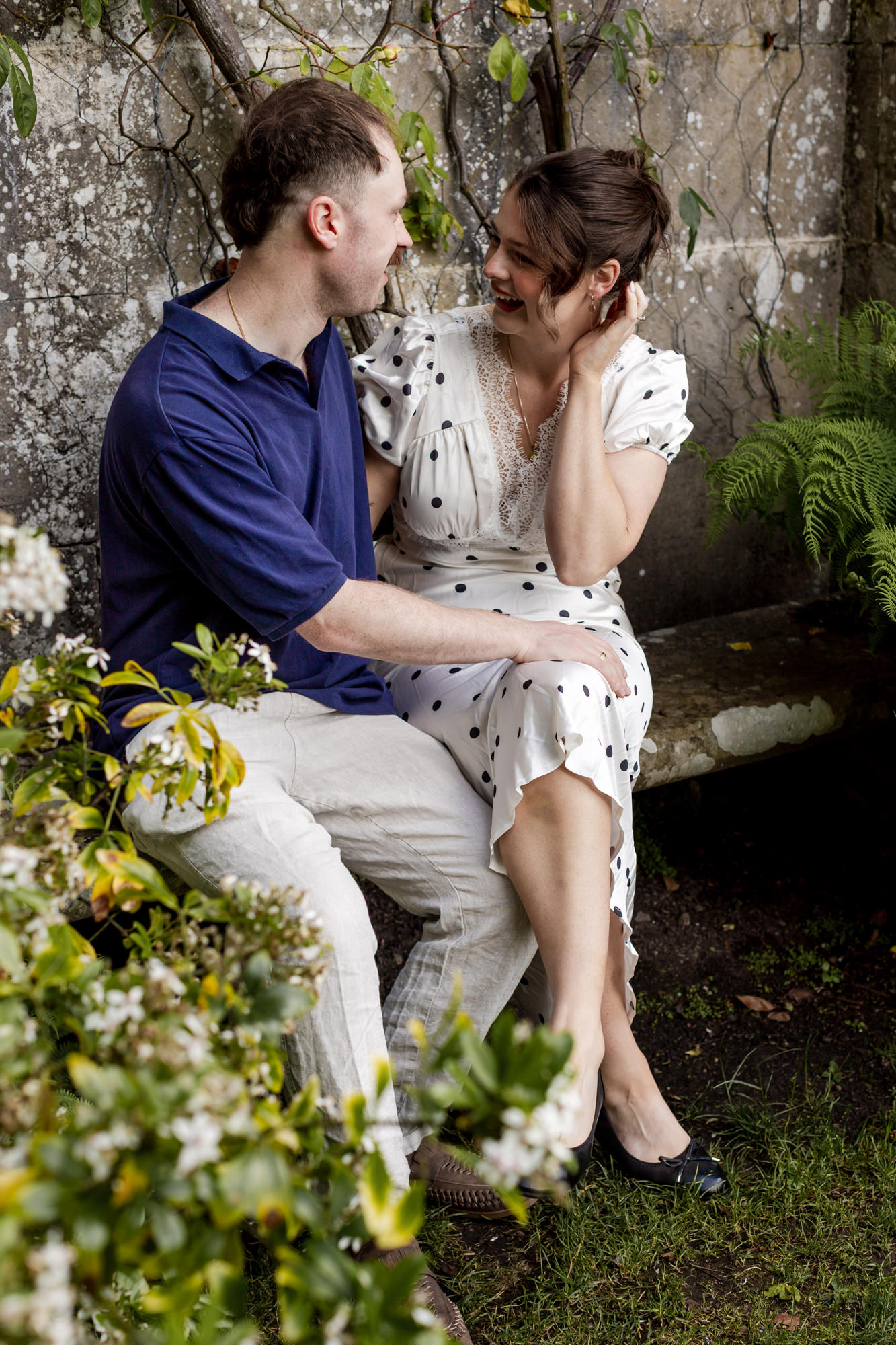 couple giggling on a stone garden bench against a wall