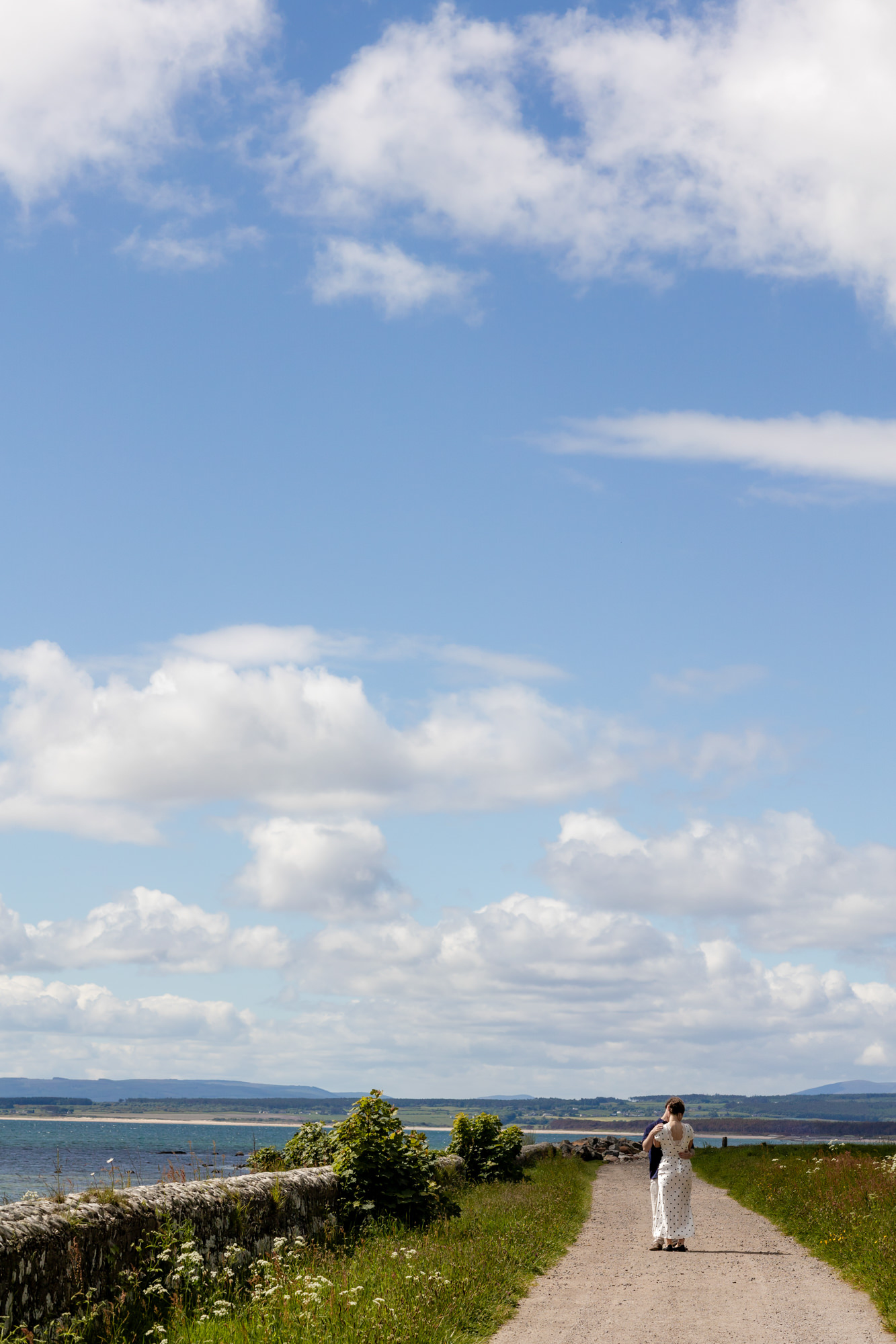 newly engaged couple embracing on a dusty track, in the summer sunshine  in the Scottish Highlands. 