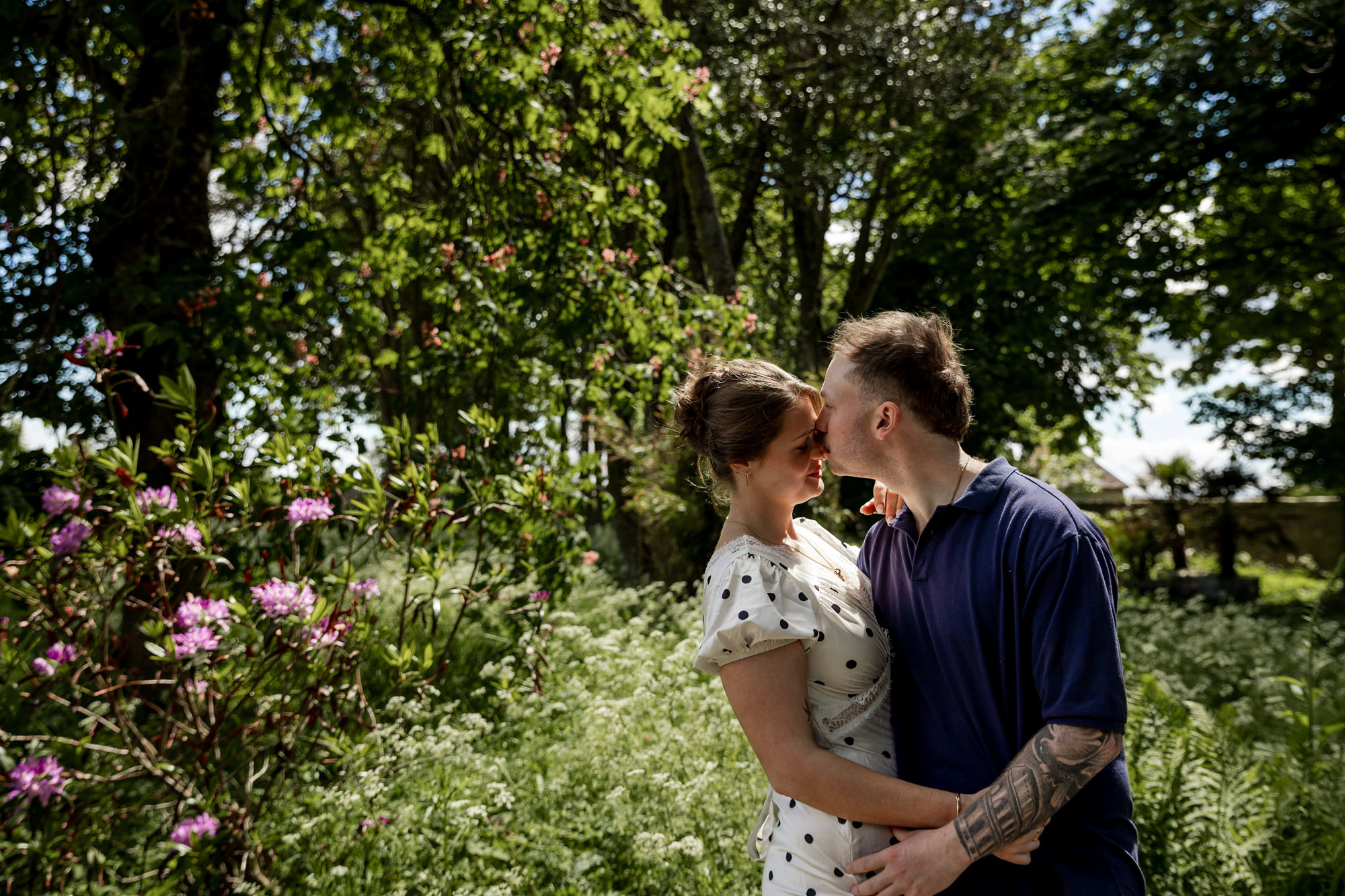 man kissing his fiancee on the forehead surrounded by garden plants and sunshine