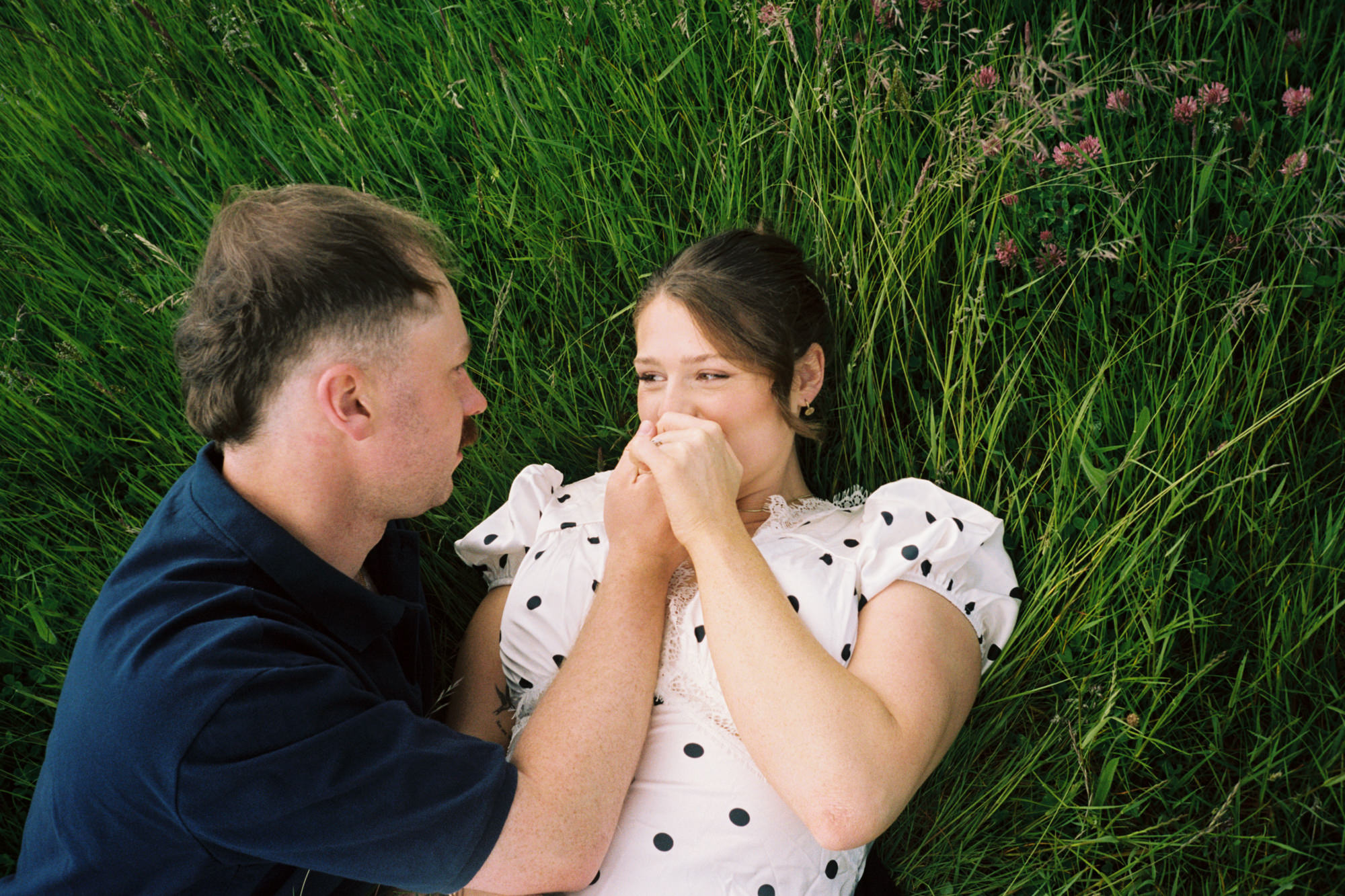 woman kissing her fiance's hand, while lying in long grass