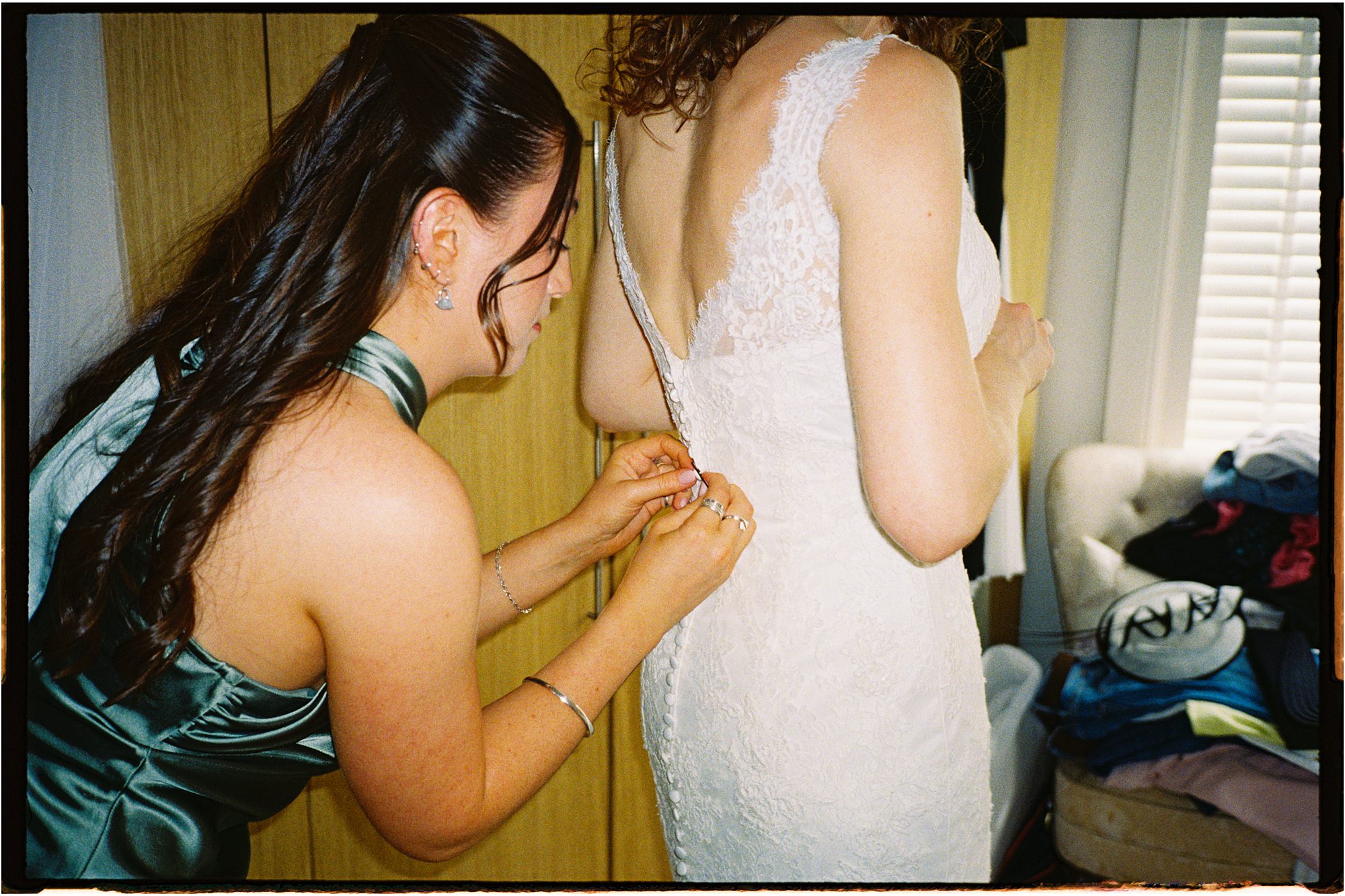 analogue photo of a bridesmaid buttoning up a brides wedding dress,